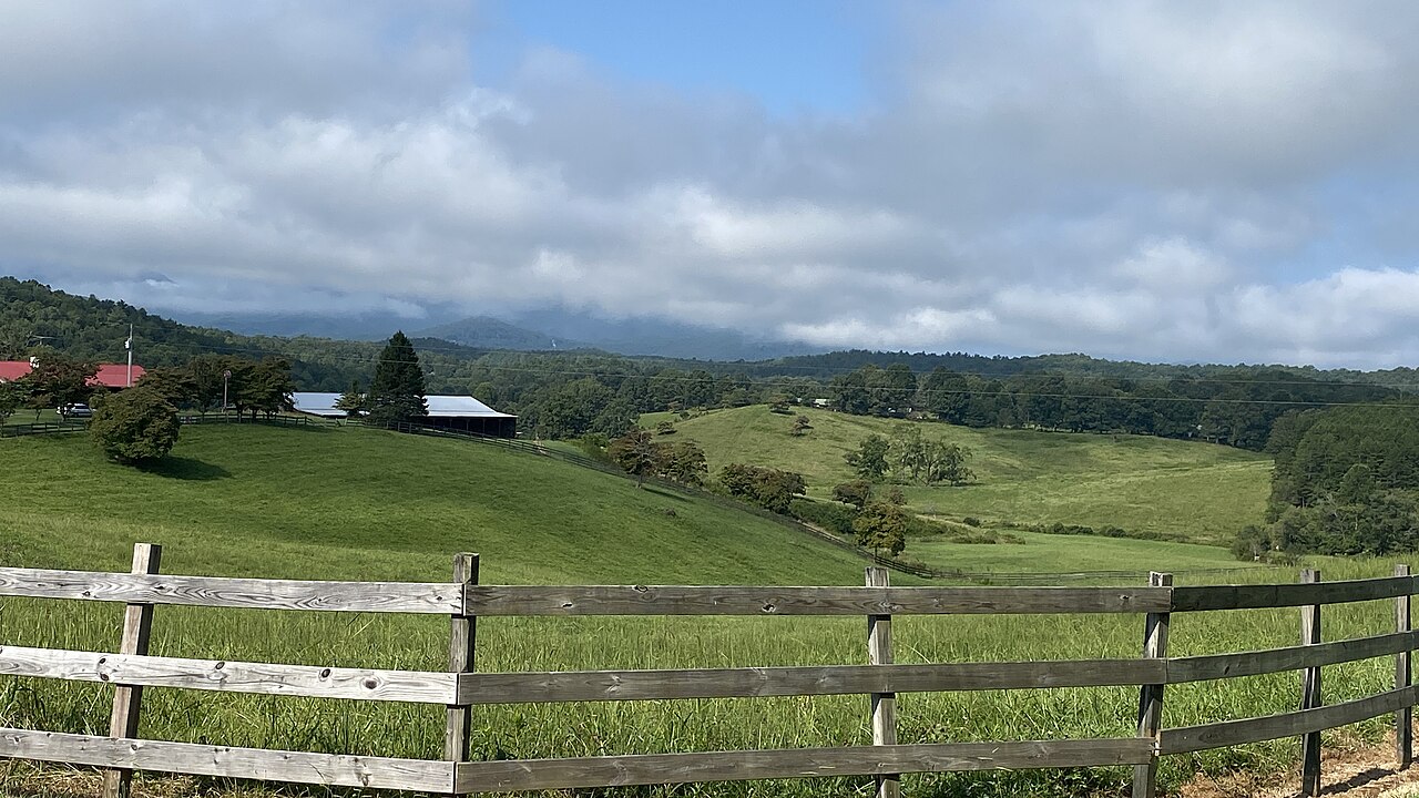 Open pasture and a split-rail fence in Fannin County, Georgia, with wooded ridgelines of the North Georgia mountains under low cloud behind