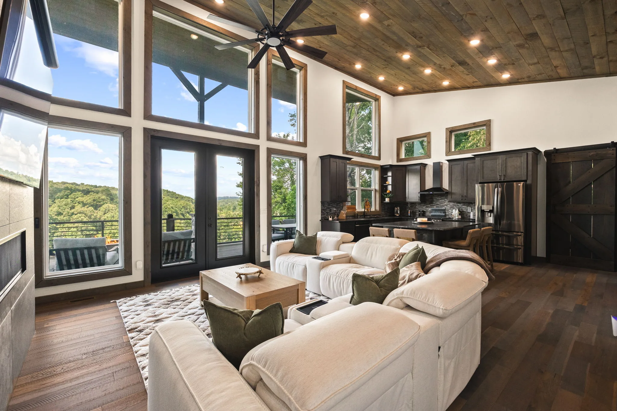 Standing in the great room looking out — glass doors open onto the covered deck and the ridgeline past it.