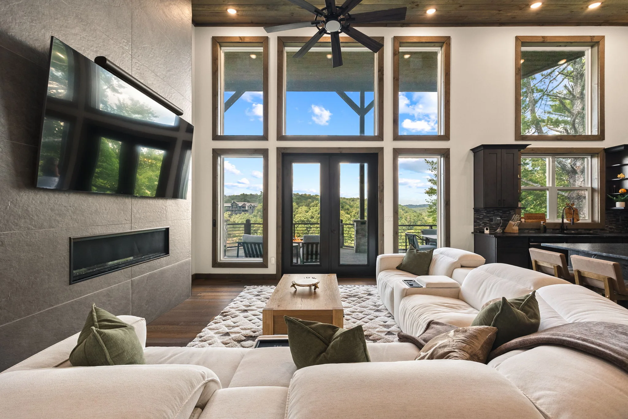 Hero view of the great room: stone-faced linear fireplace, television above, and the window wall carrying the view in.