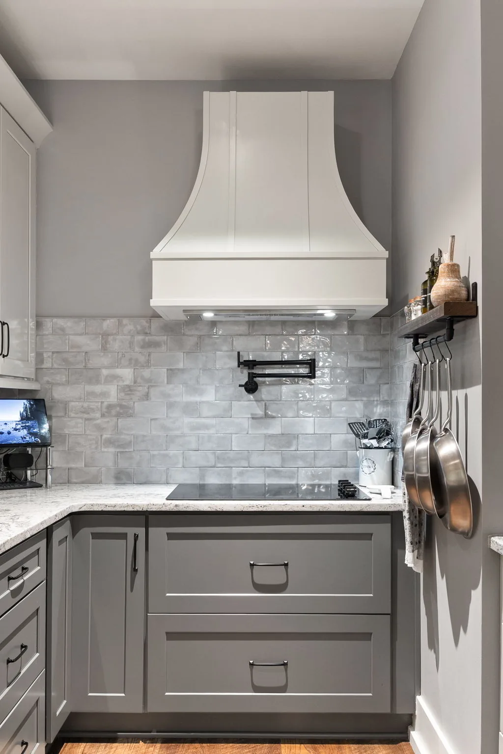 Detail: vent hood, pot filler and electric glass cooktop over the tile backsplash