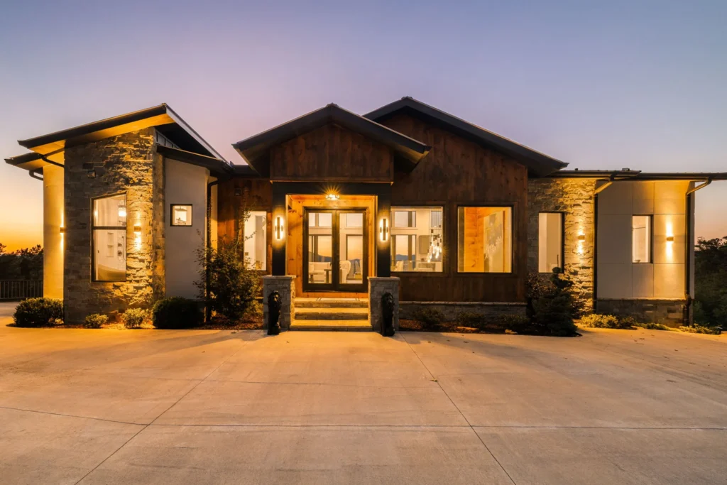Front elevation at twilight, warm interior glow behind stacked-stone columns