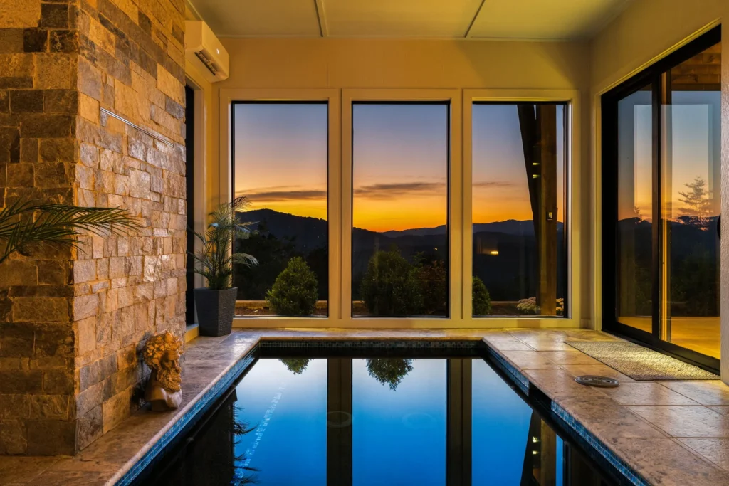 Indoor pool at sunset, travertine deck and stacked-stone wall against a mountain sky