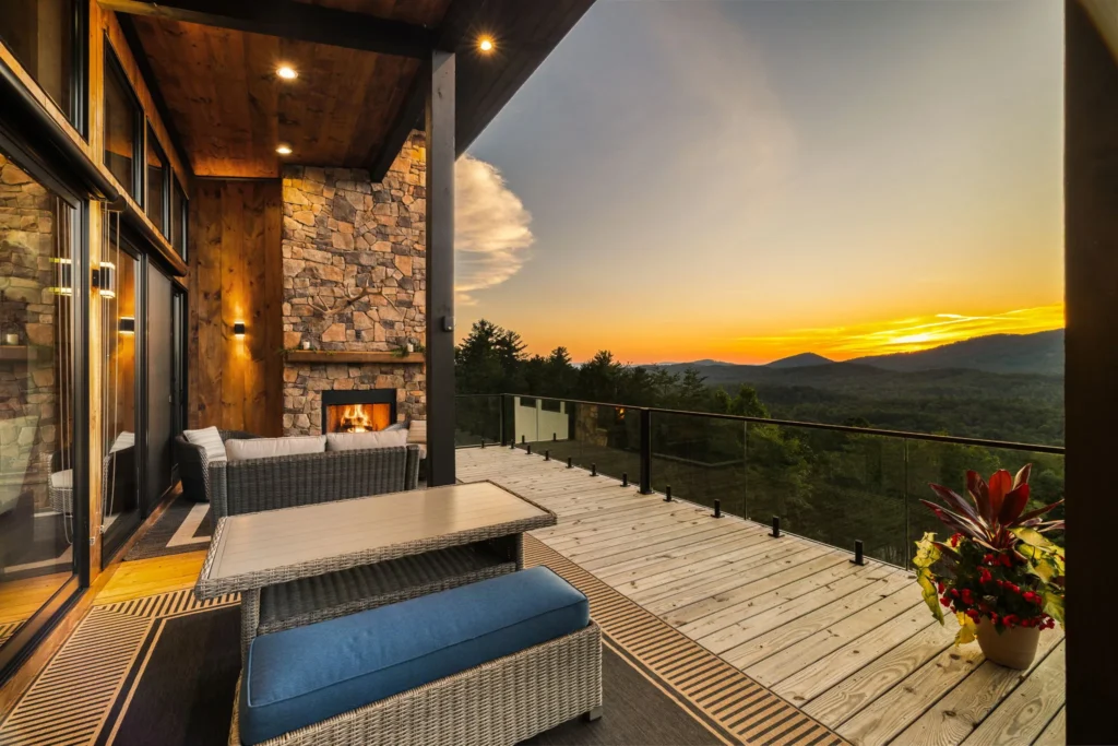 Outdoor stone fireplace lit on the deck at sunset, wicker seating and cable railing