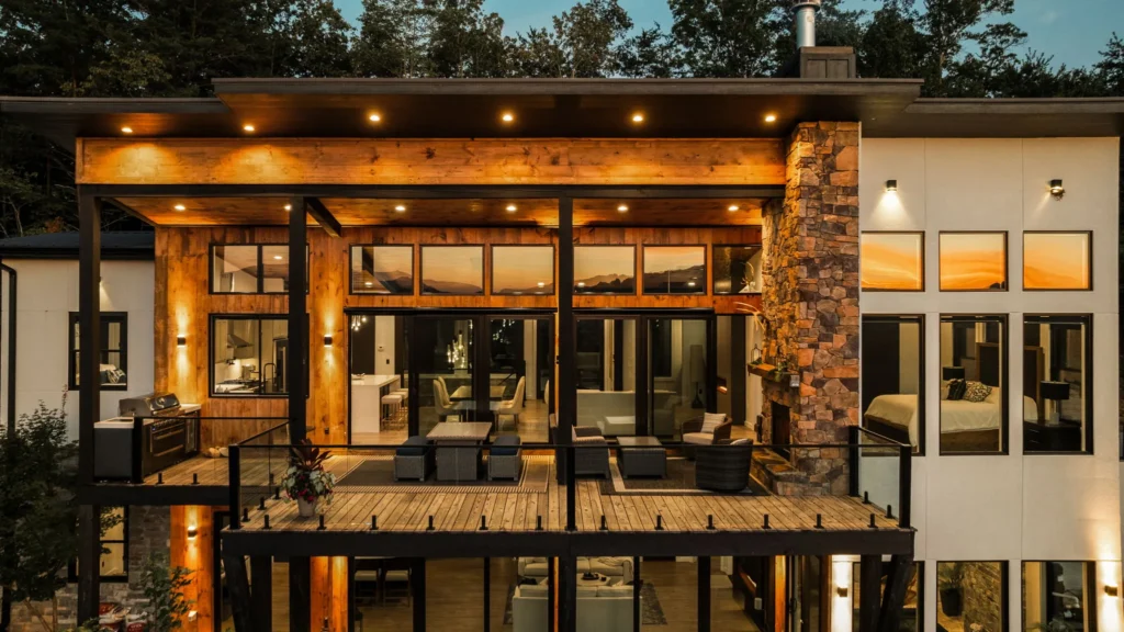 Drone view of the rear elevation at dusk, interior glowing and the outdoor fireplace lit