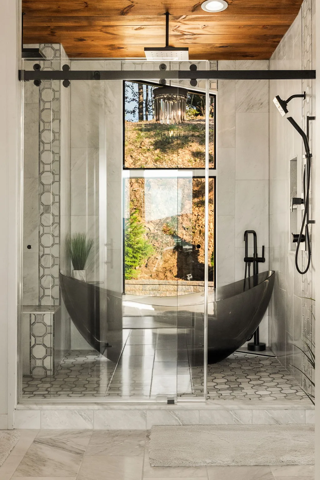 Freestanding soaking tub behind glass, marble tile and matte black fixtures