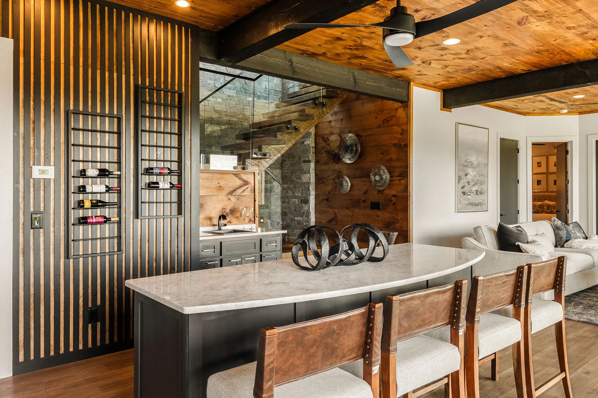 Terrace-level wet bar: curved marble island, leather barstools and a slatted wine wall