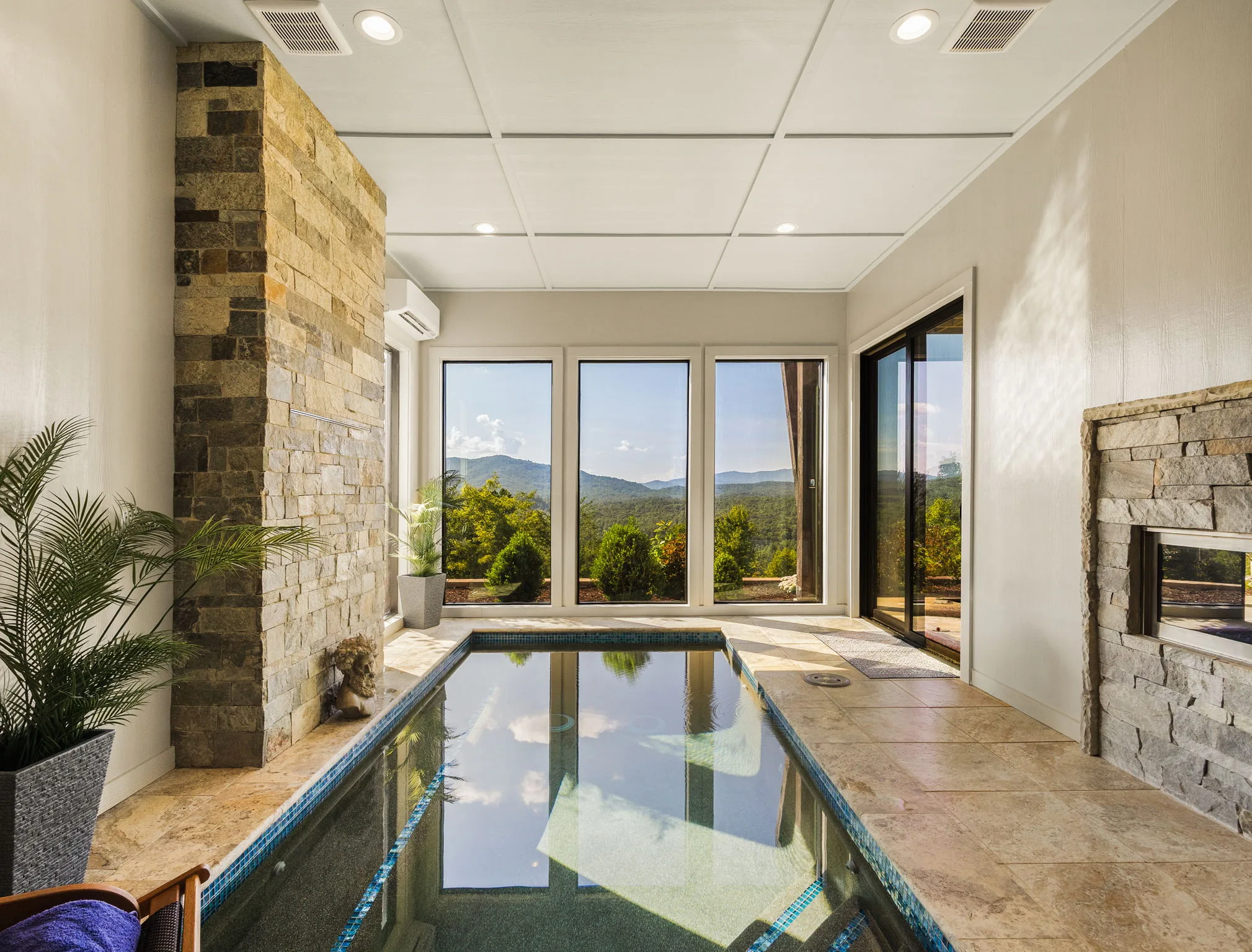Indoor pool with a stone fireplace surround and floor-to-ceiling windows