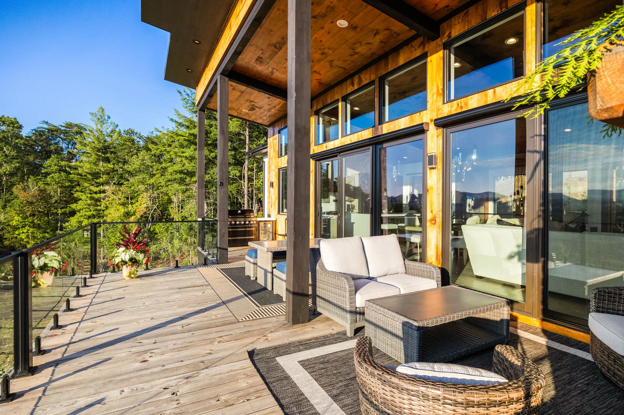 Covered deck with wicker seating, cable railing and a wood ceiling over the tree line