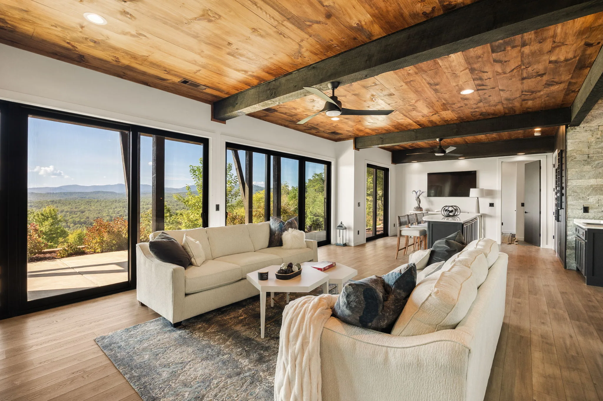 Terrace-level family room: cream sectionals under a wood-and-beam ceiling, black-frame sliders onto the mountain view