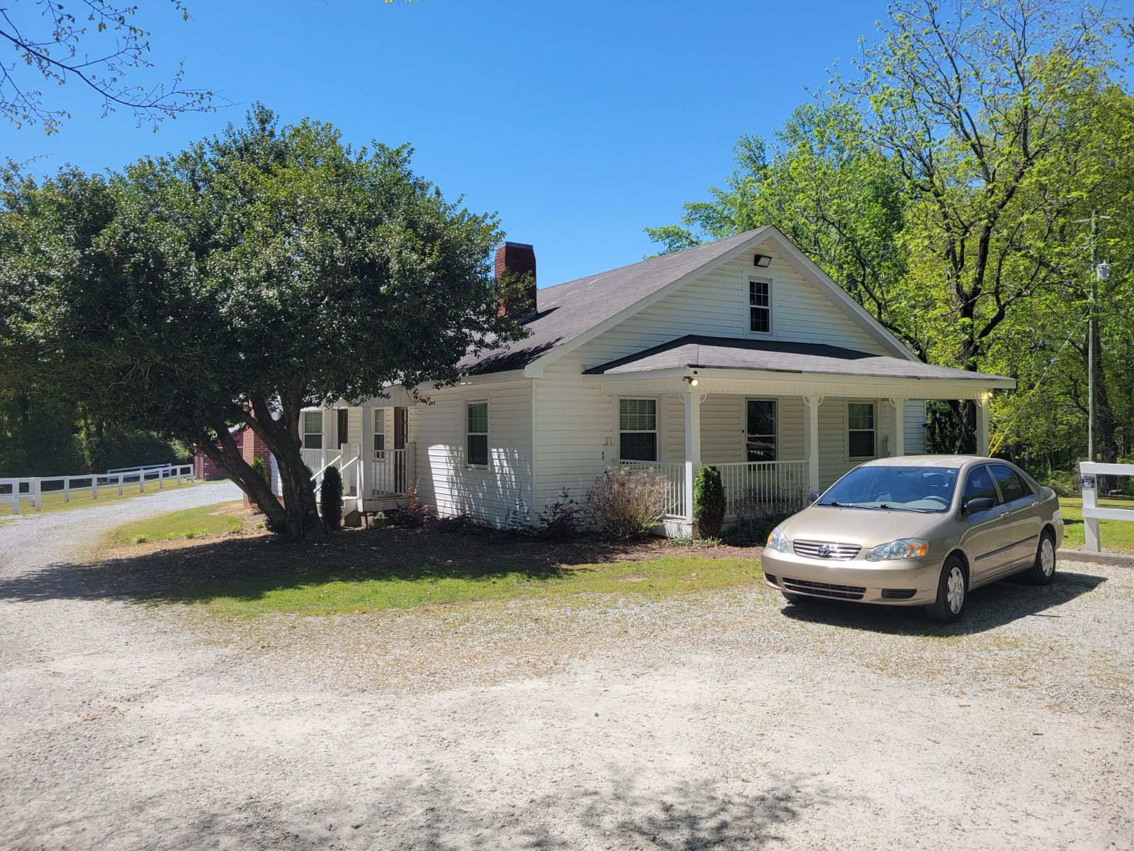 White one-story farmhouse with a covered front porch, a gravel drive and a parked sedan at Clinton Nature Preserve in Douglas County, Georgia