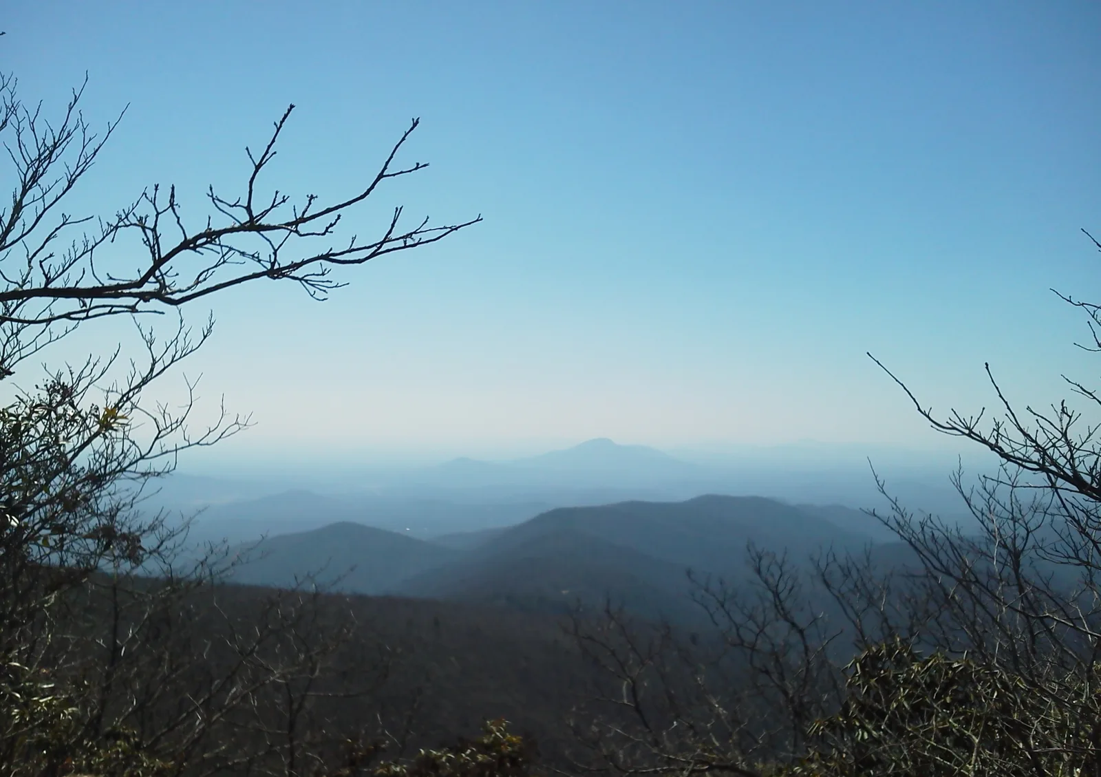 Layered blue ridgelines of the North Georgia mountains seen from Tray Mountain on the Appalachian Trail, framed by bare winter branches