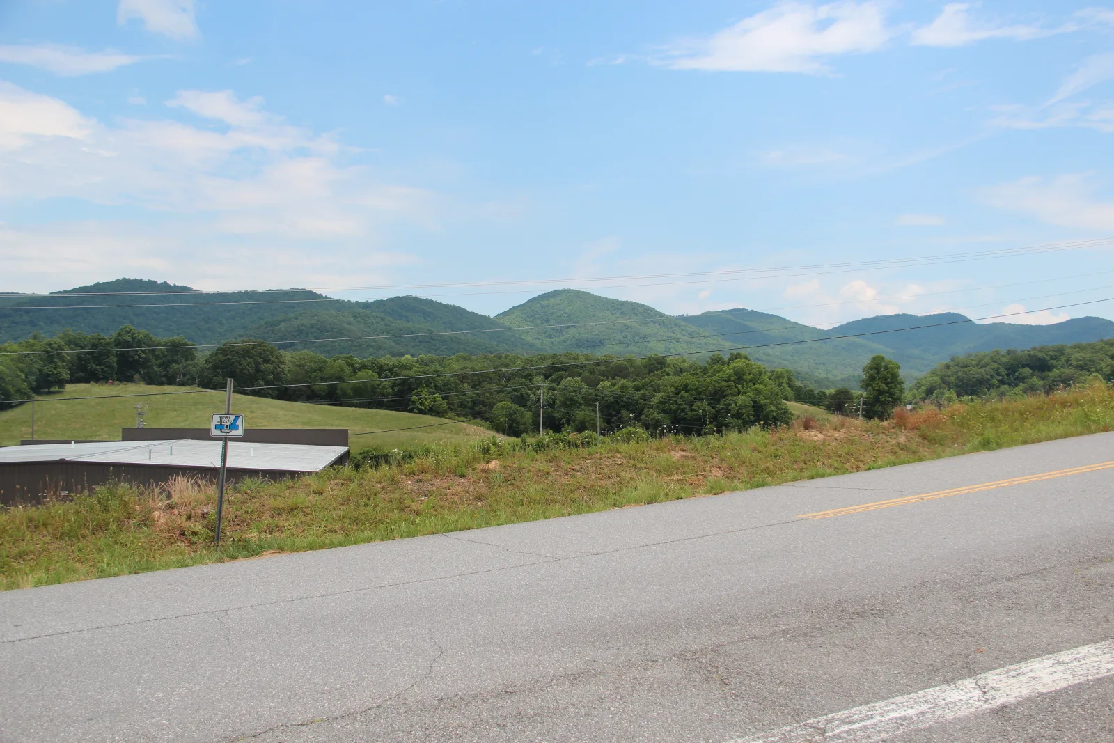 Forested mountains in Union County, Georgia, rising behind open pasture, a paved road, and roadside power lines under a summer sky