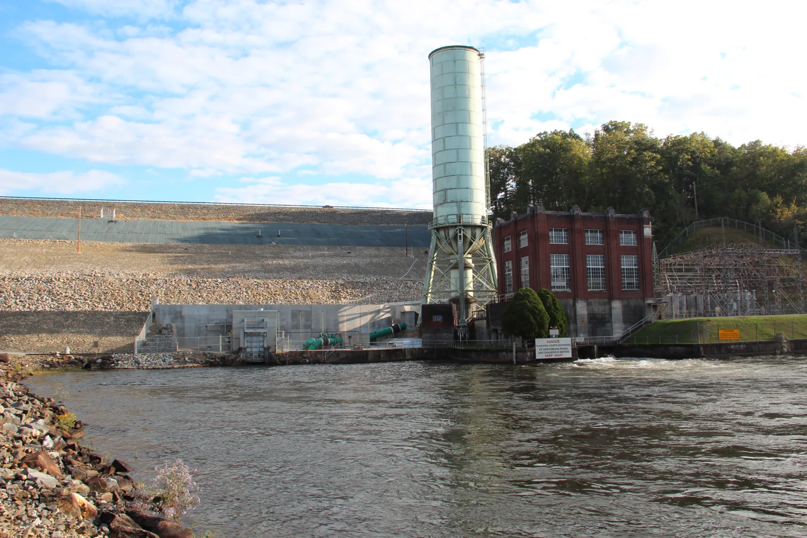 The Toccoa River tailwater below Blue Ridge Dam in October, with the powerhouse, intake tower, and rock face of the dam behind the current