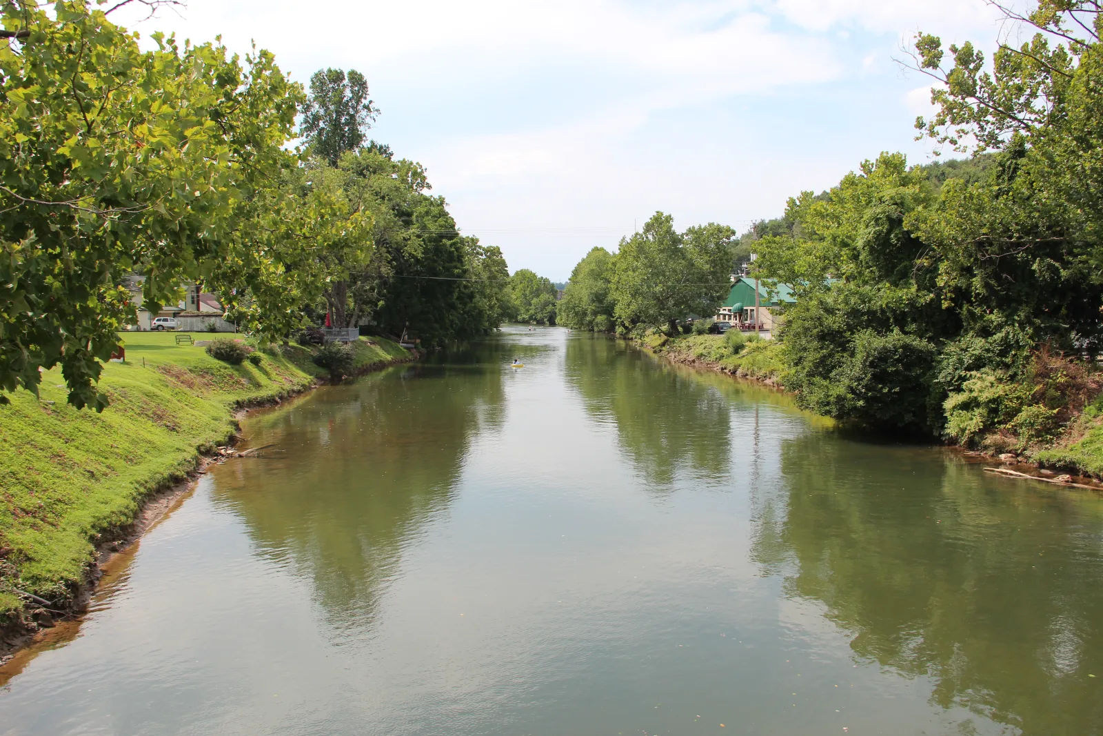 The Toccoa River at McCaysville in July, downstream of Blue Ridge Dam, with grassy banks, shade trees, and a single tuber far down the current