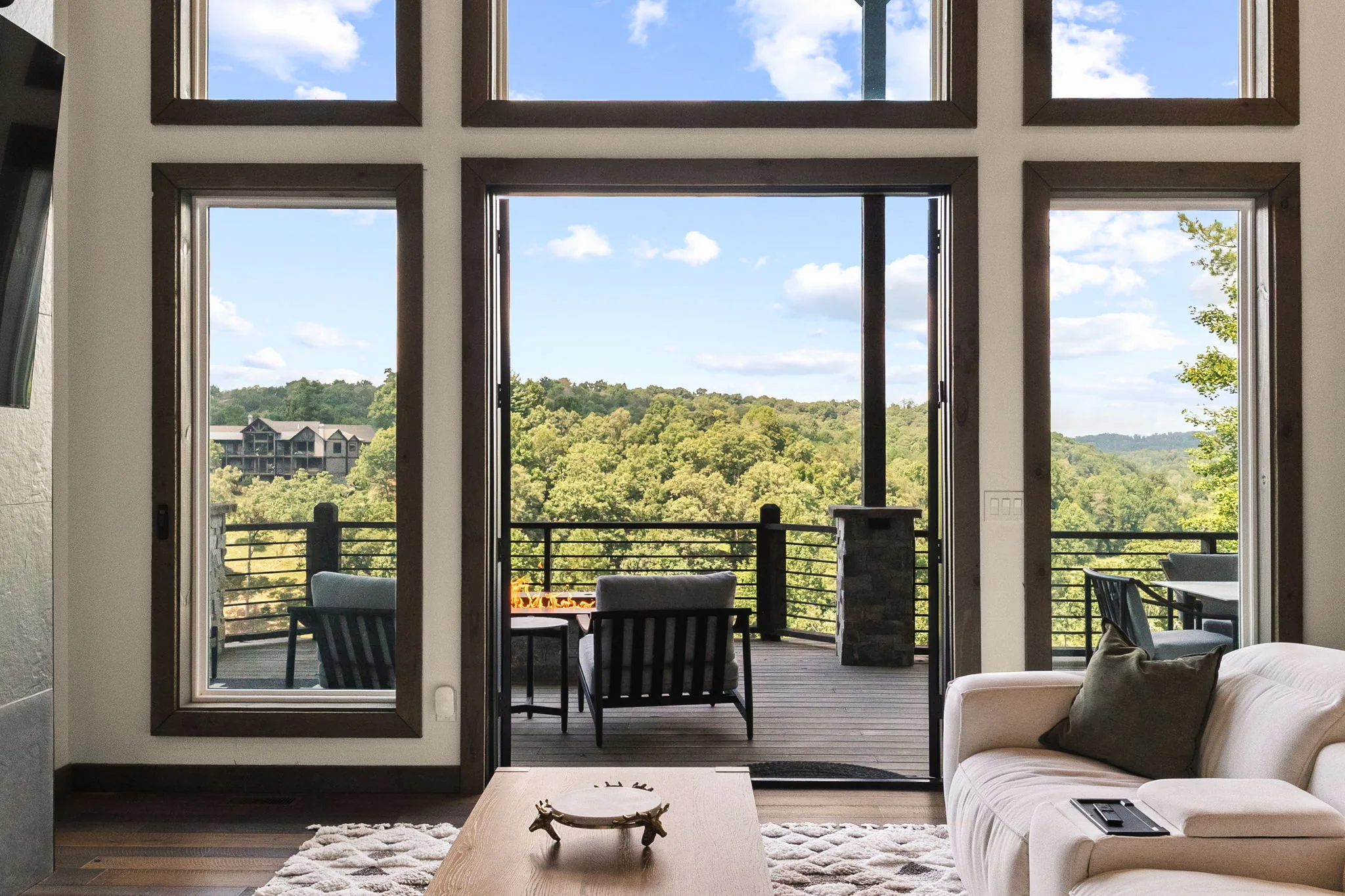 Great room with the two-storey glass wall folded open onto the covered deck and the mountains beyond