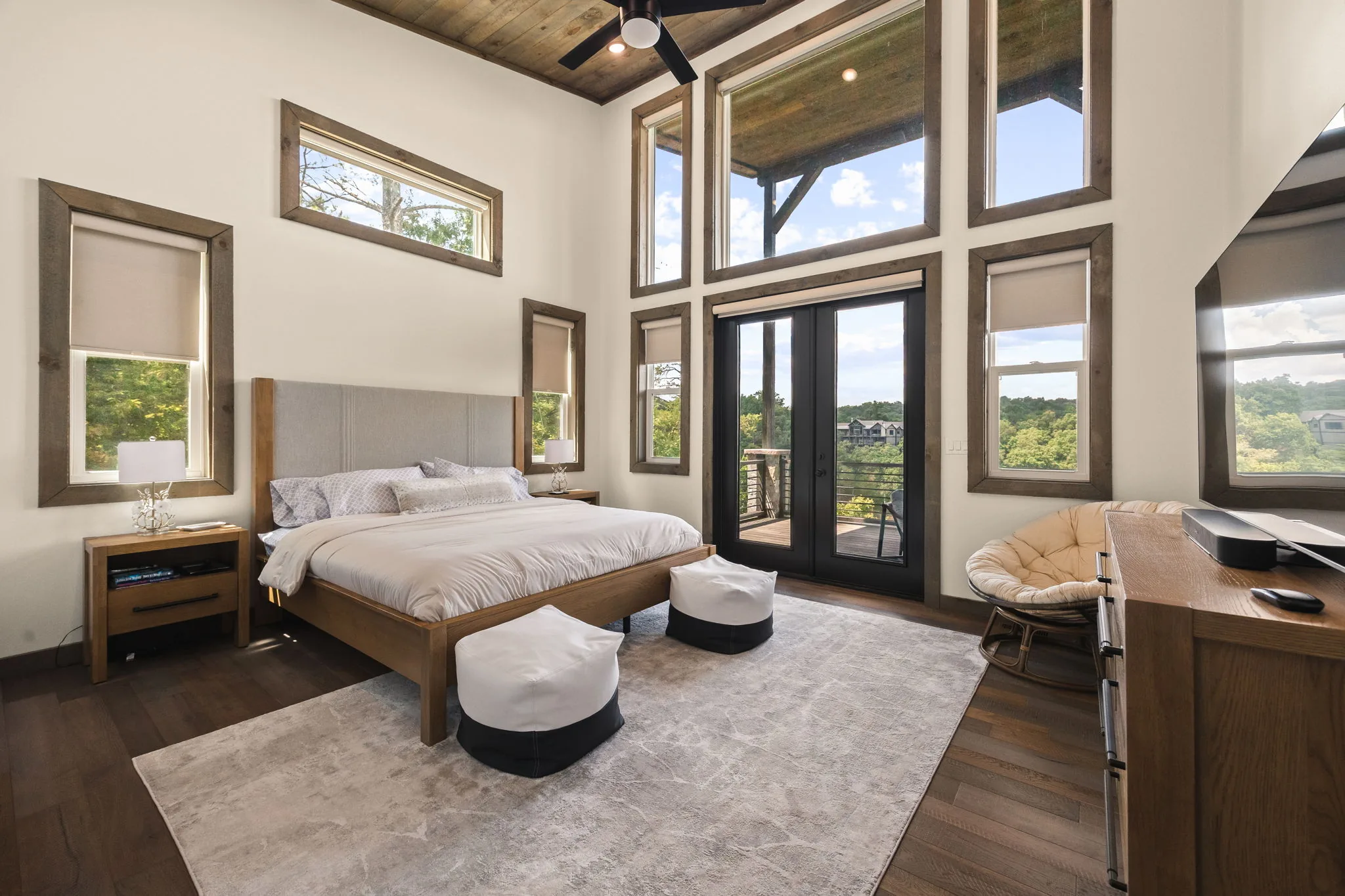 The primary bedroom on the main level, with a two-story window wall and private door onto the deck.