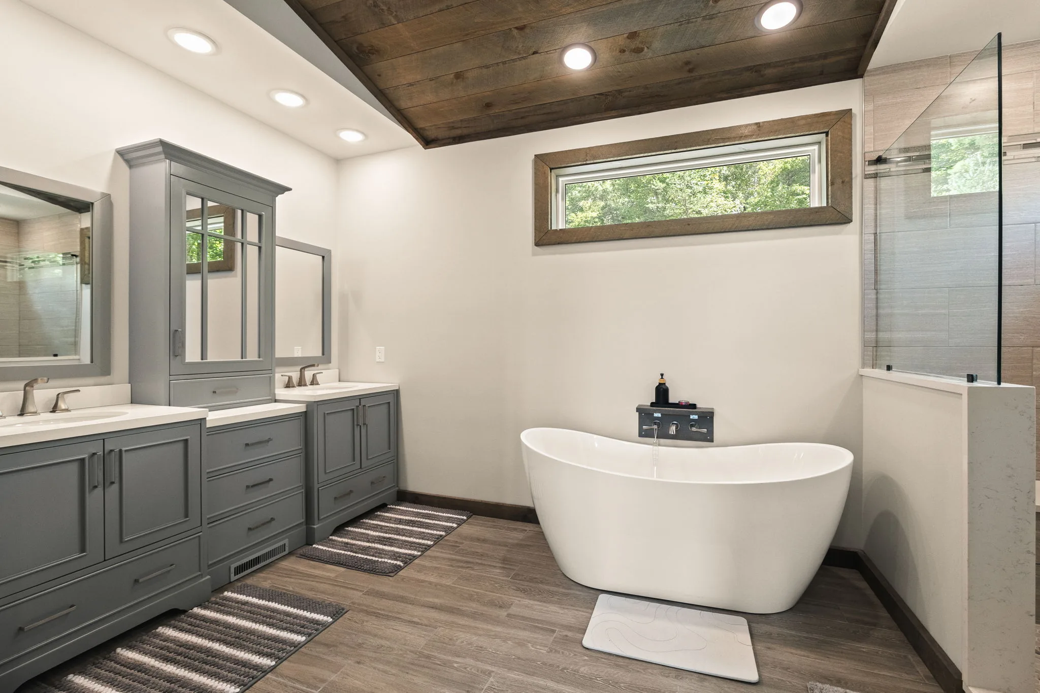 The primary ensuite in full — double vanity, freestanding soaking tub and a glass walk-in shower under a shiplap ceiling.