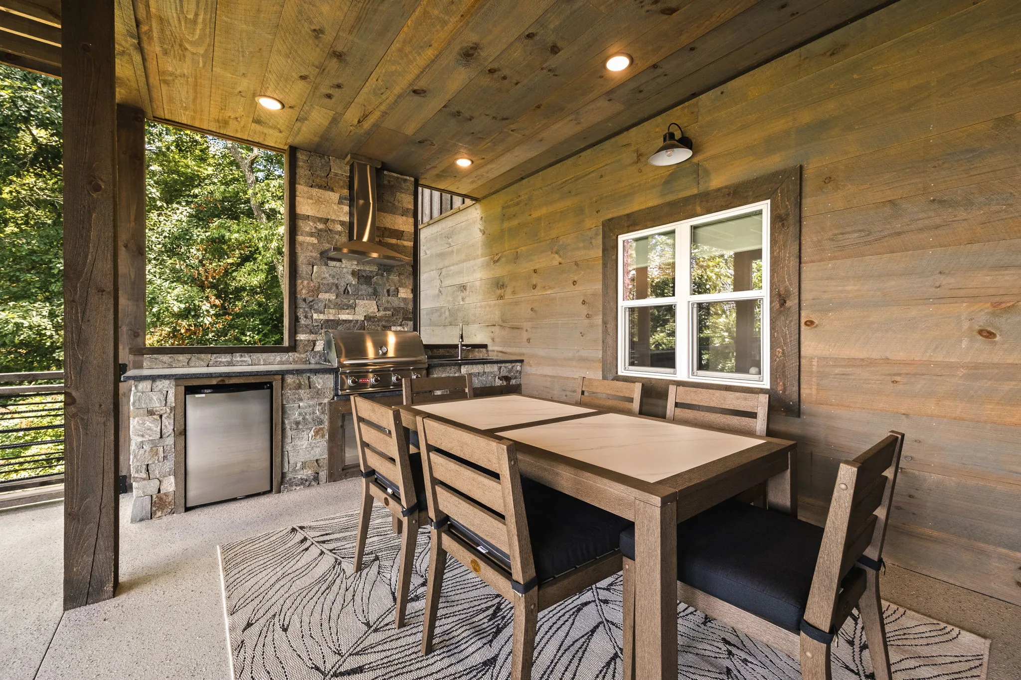 Lower covered patio with a stone outdoor kitchen and outdoor fireplace under a timber ceiling