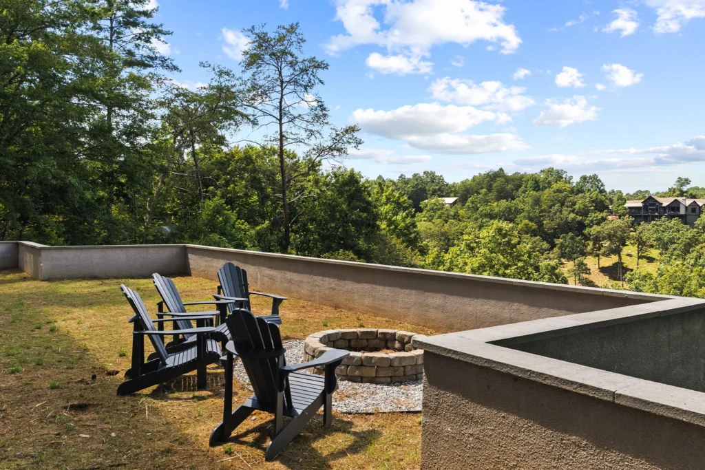 Stone fire pit ringed with Adirondack chairs on the terraced lawn below the house.